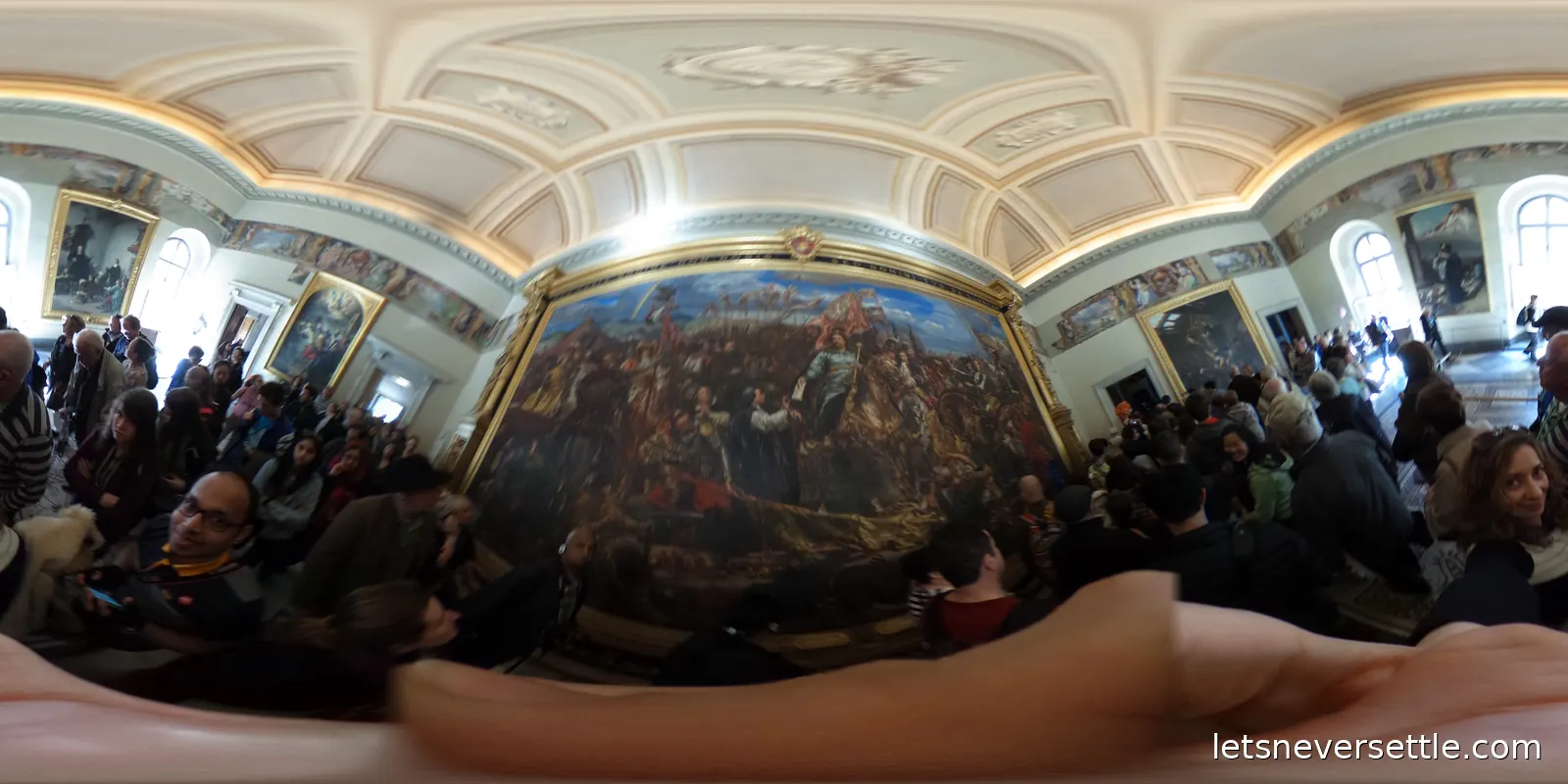 A gallery hung with a vast battle painting, framed portraits along the side walls and a crowd of visitors packed in front of it