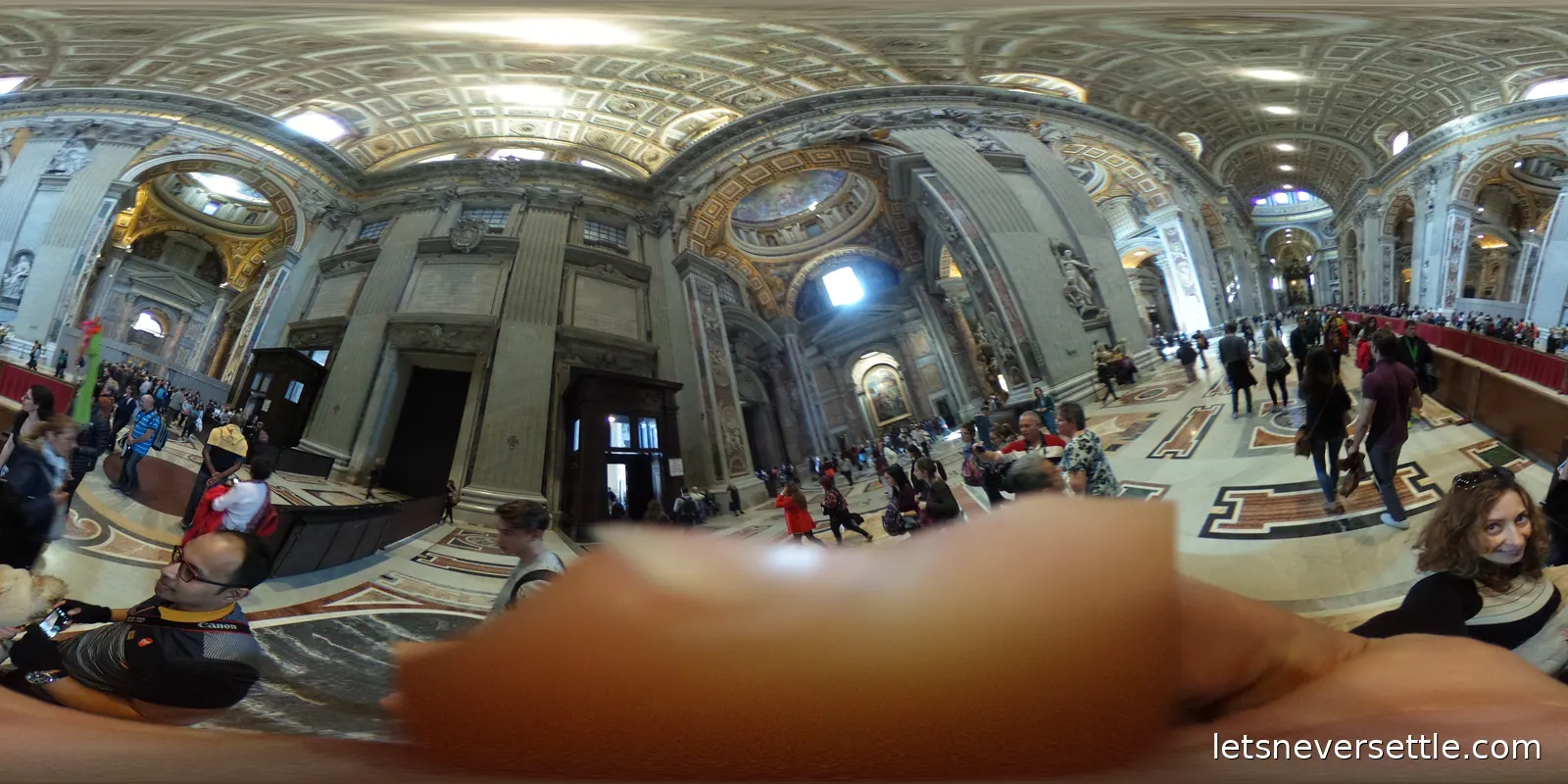 The side aisles and nave of St Peter's Basilica seen in every direction, with gilded vaults, marble statues and visitors crossing the patterned floor