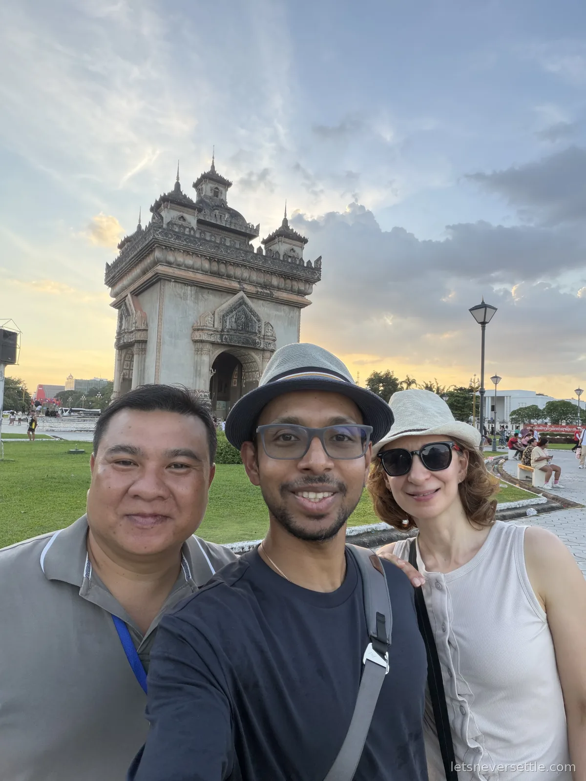 Selfie of Dileep and Inga with a smiling companion in front of Patuxai at golden hour