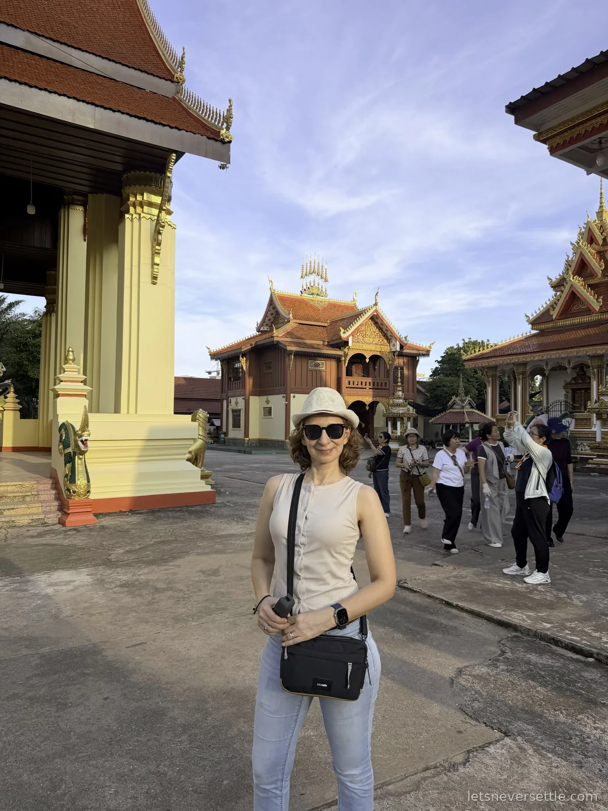 Inga in a sun hat standing in a temple courtyard with a wooden pavilion behind her and a tour group walking past in the afternoon sun