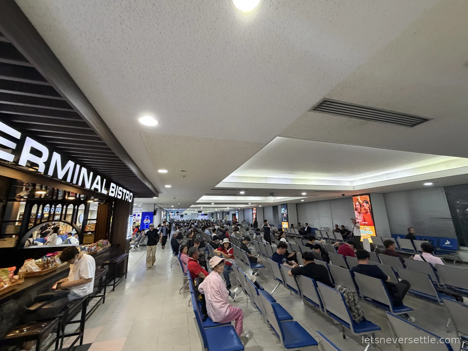 Rows of blue seats filling the departures hall at Wattay airport in Vientiane late at night, with a Terminal Bistro counter along the left wall