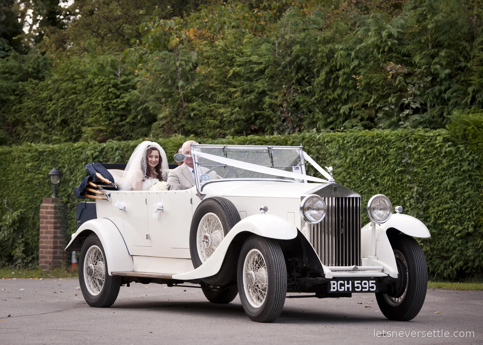 Inga in her veil riding in the open-top white vintage Rolls-Royce with white ribbons over the bonnet