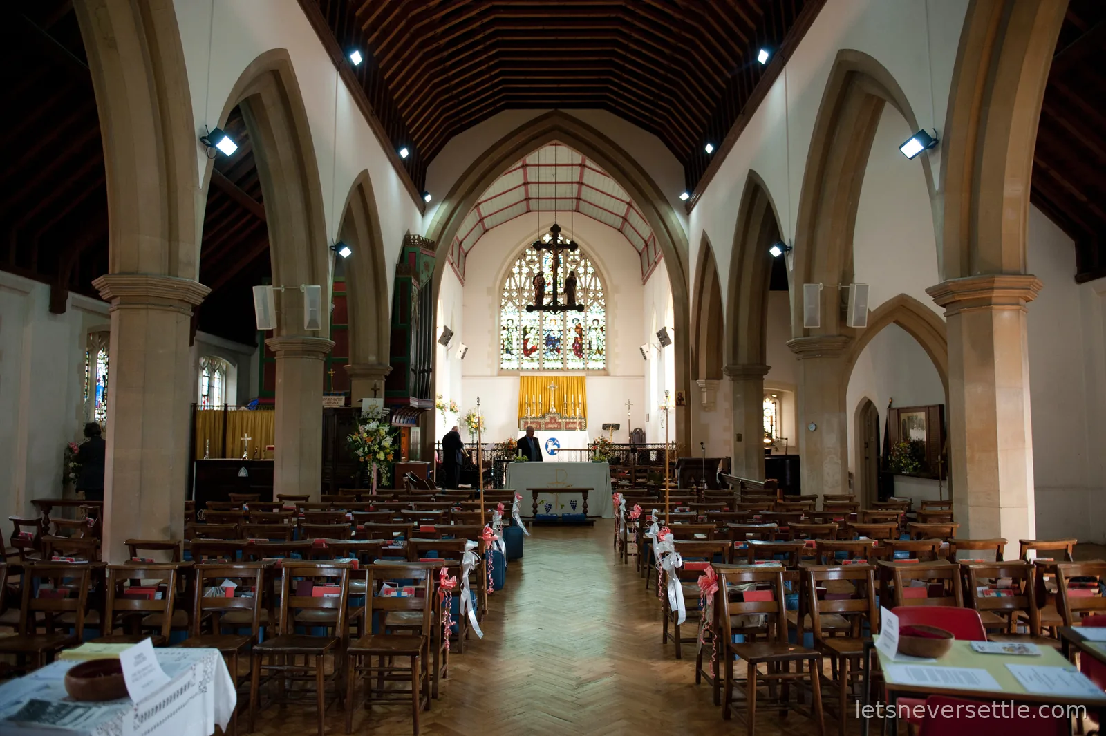 The nave of the church before the ceremony, stone arches and wooden chairs decorated with ribbons, flowers by the altar