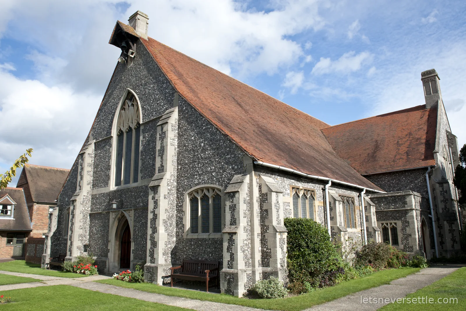 A flint church with a steep red tiled roof, stone-traced Gothic windows and a small bellcote, under a blue October sky