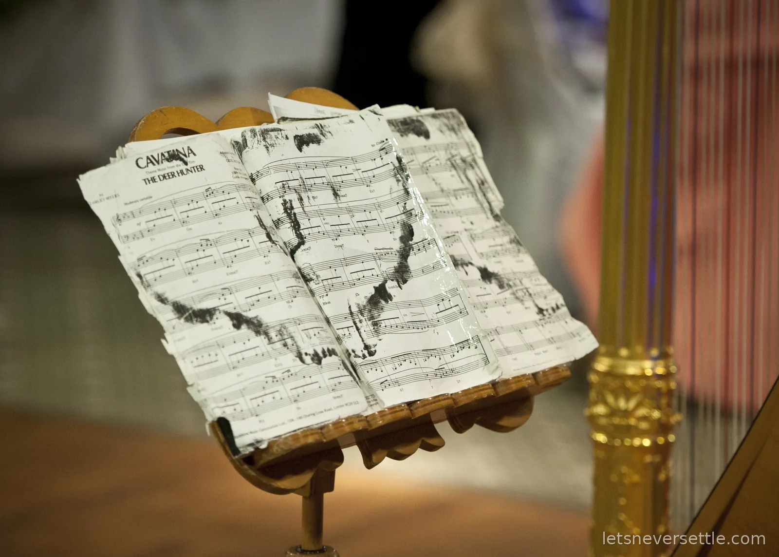 Well-worn sheet music for Cavatina, the theme from The Deer Hunter, on a stand beside a gilded harp