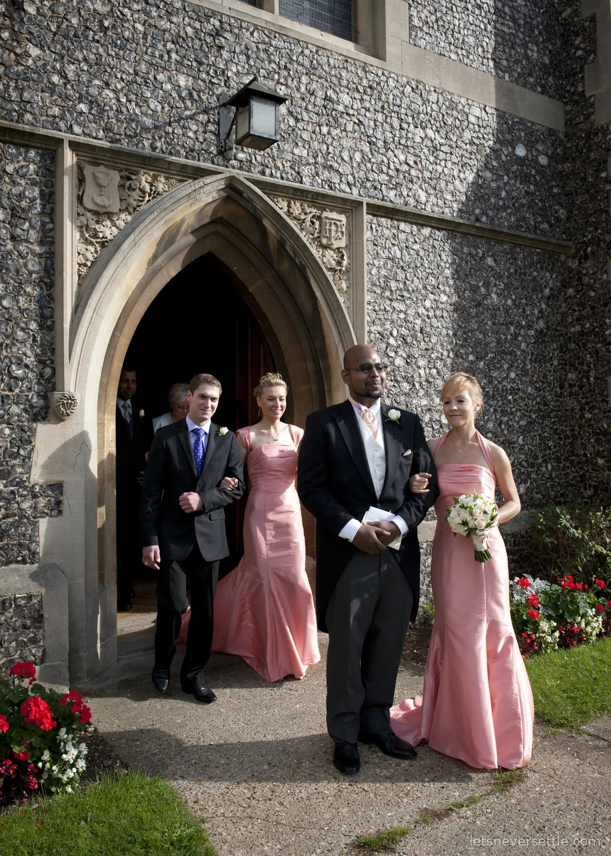 Dileep in his tailcoat leading Inga's bridesmaids and family out of the church door past beds of red flowers