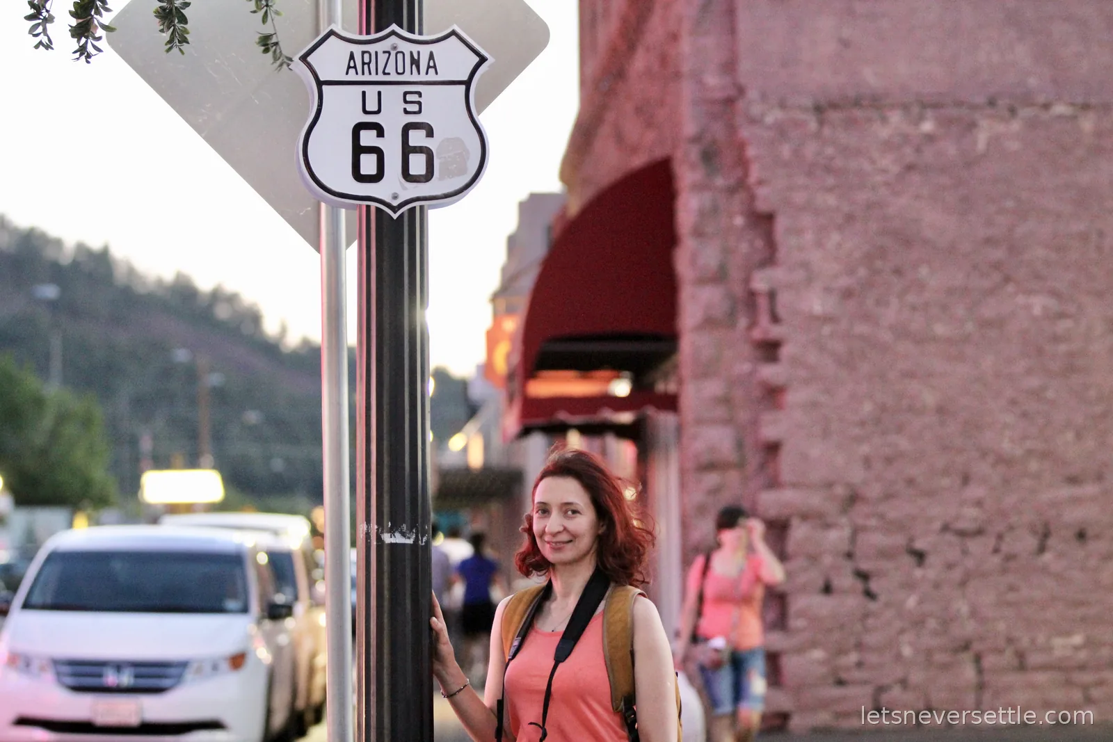 Inga holding a signpost under a white Arizona US 66 route shield on the main street of Williams