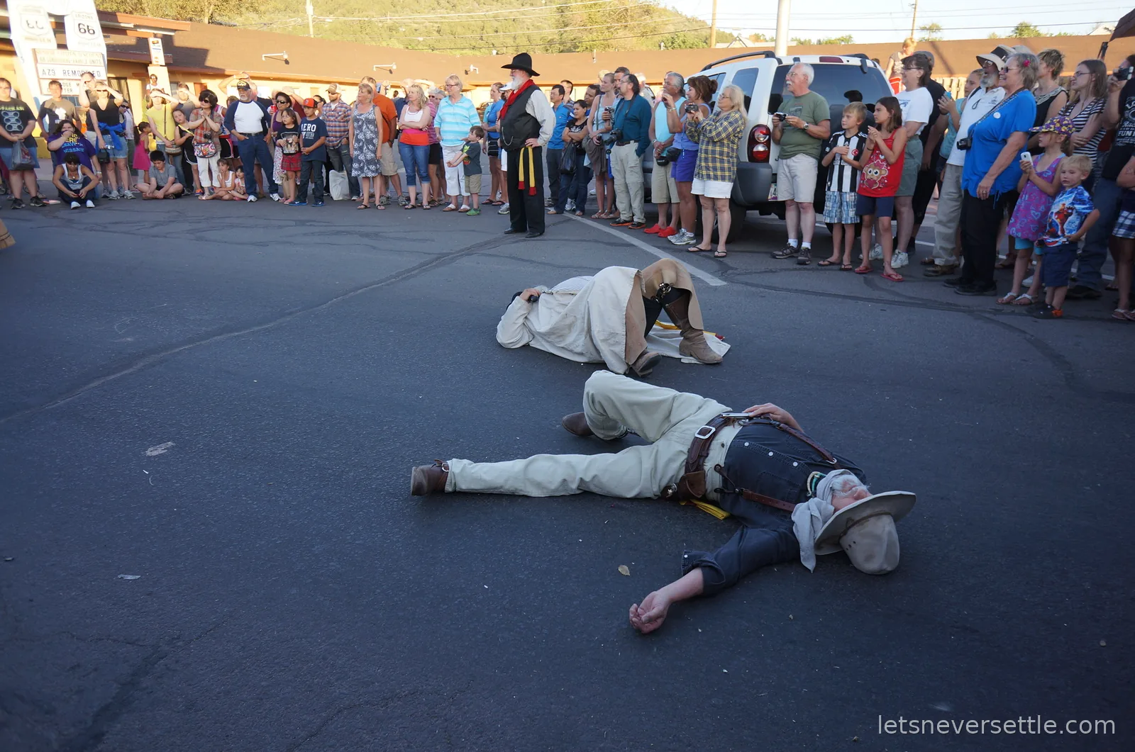 Costumed outlaws lying flat on the tarmac after the staged gunfight while the crowd looks on