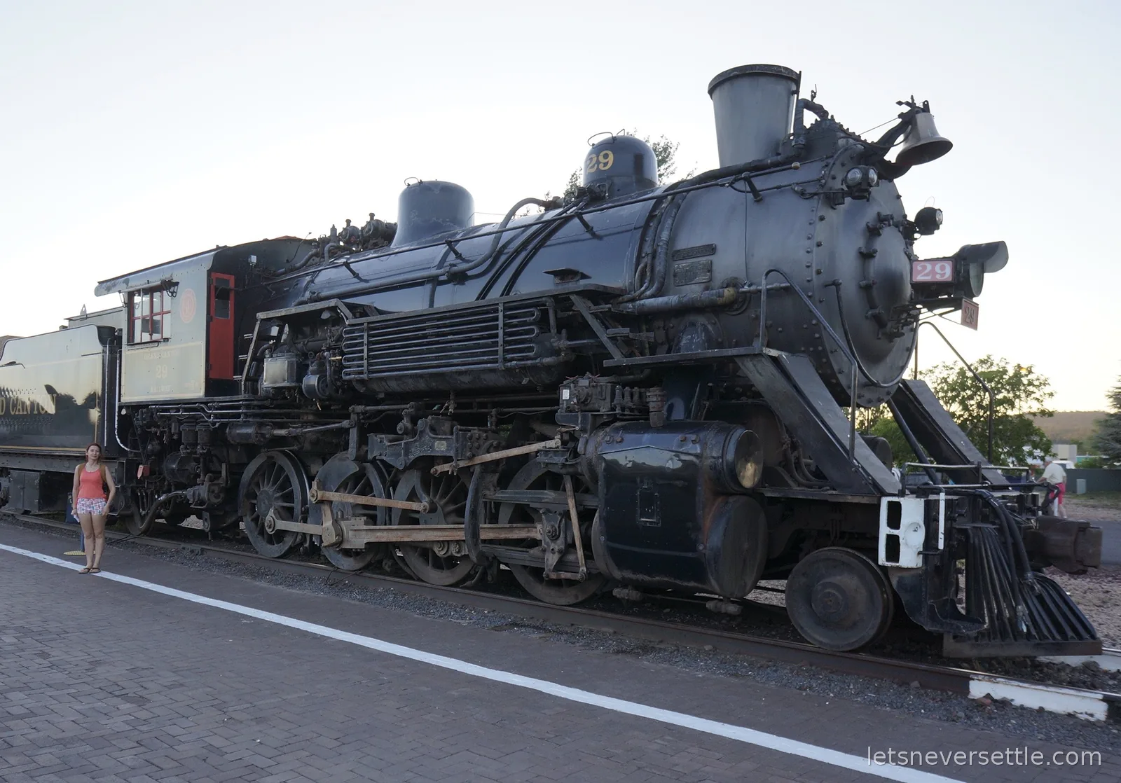 Black steam locomotive number 29 of the Grand Canyon Railway on static display, with Inga standing by its driving wheels for scale