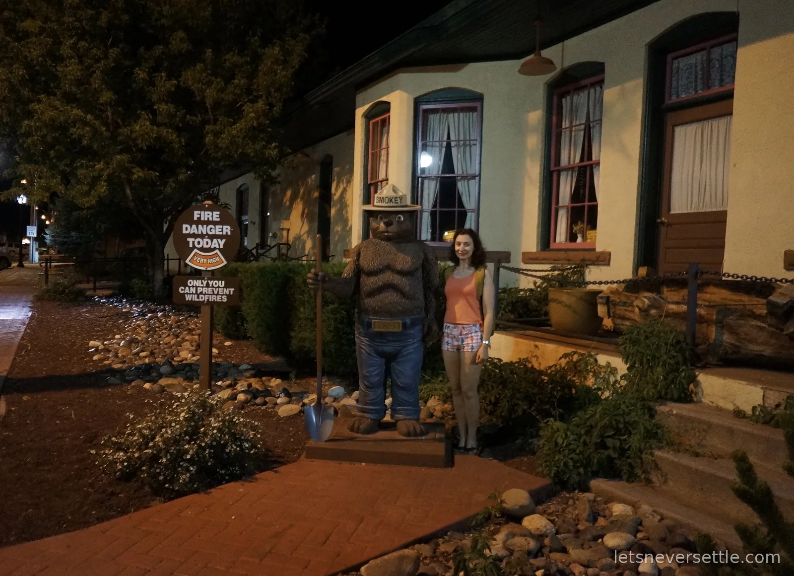 Inga next to a carved Smokey Bear statue holding a shovel, beside a fire danger sign at night