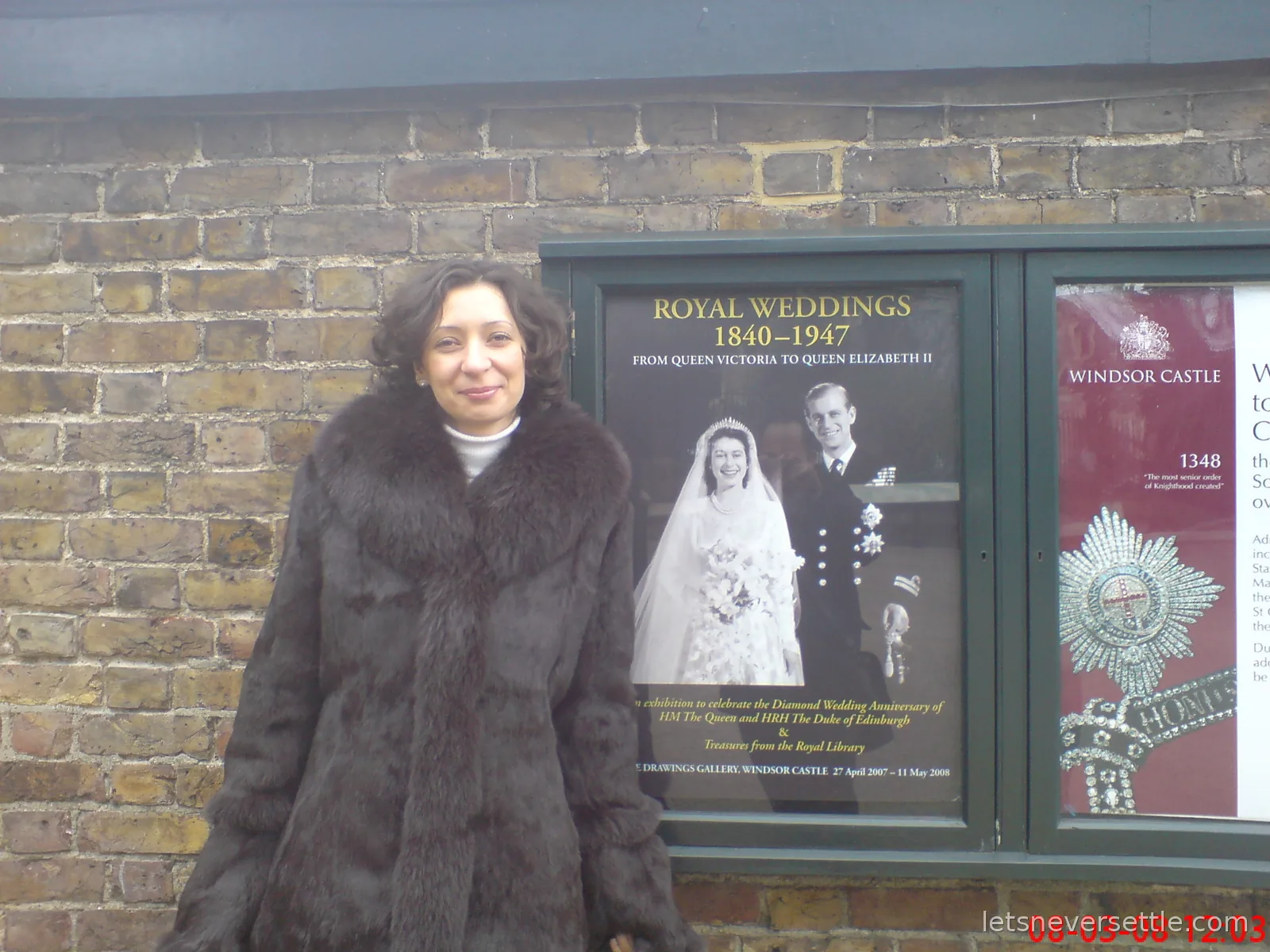 Inga in a dark fur-collared coat beside a Royal Weddings 1840 to 1947 exhibition poster on a brick wall at Windsor Castle