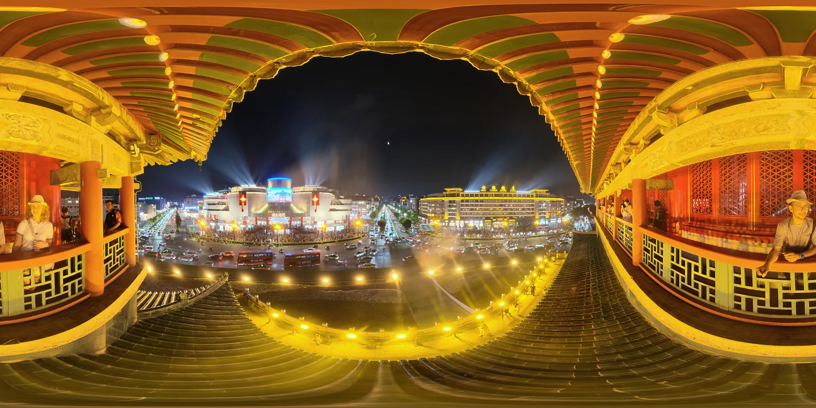The floodlit roundabout and traffic at the centre of Xi'an at night, seen from the Bell Tower balcony beneath painted green and red eaves