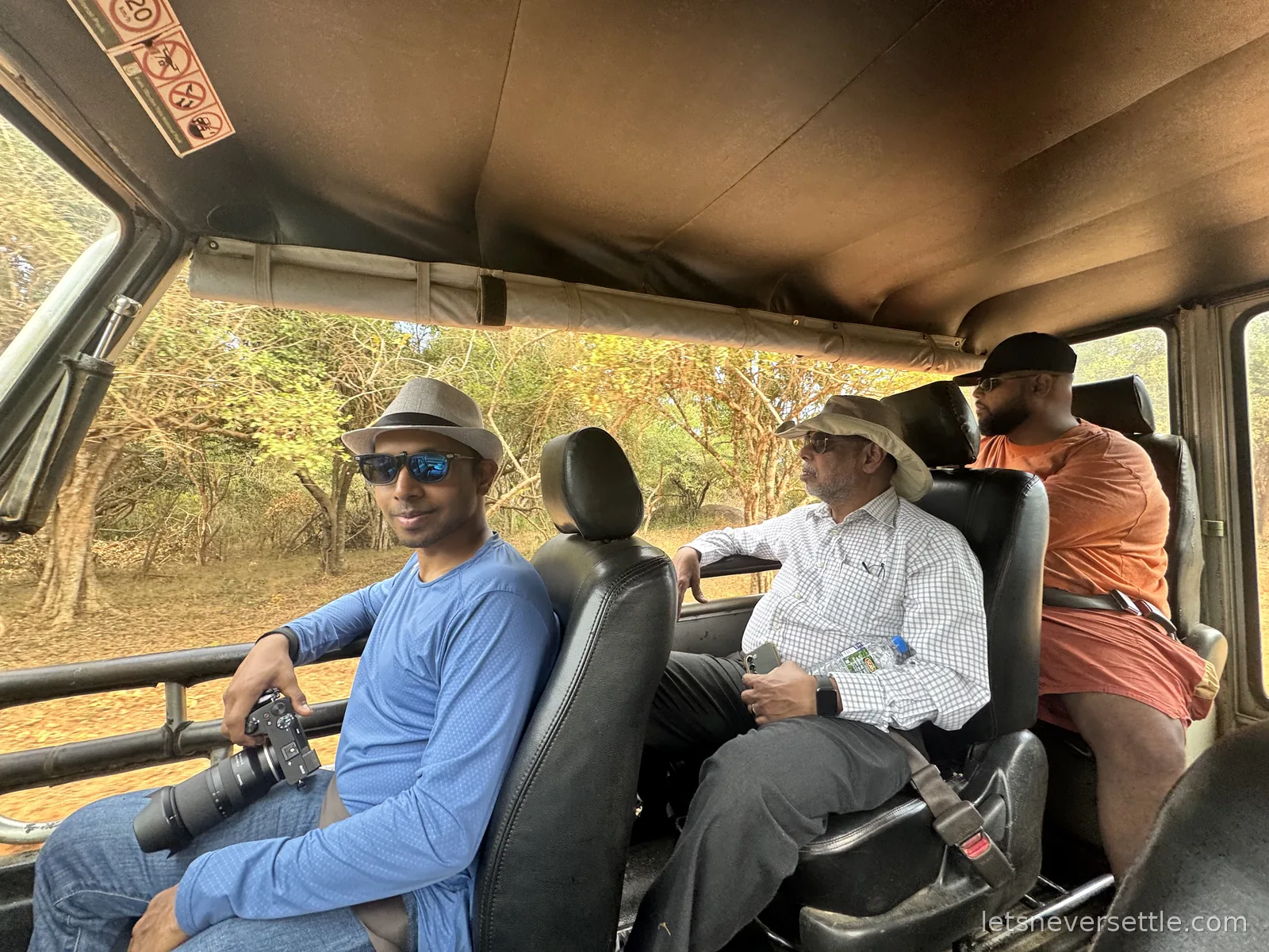 Dileep holding a camera with a long lens inside a safari jeep, with family members looking out at the dry forest