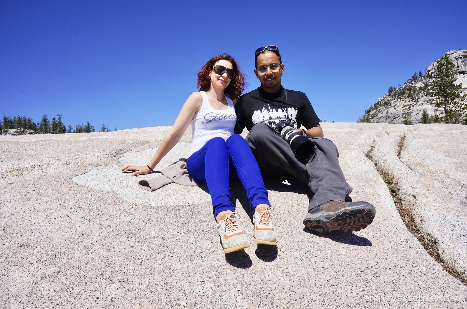 Inga and Dileep sitting together on smooth pale granite slabs under a deep blue sky