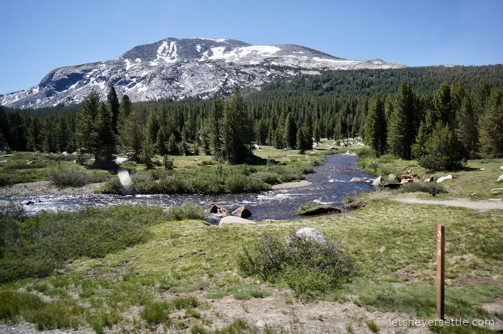 A river winding through an alpine meadow below a snow streaked mountain beside Tioga Road
