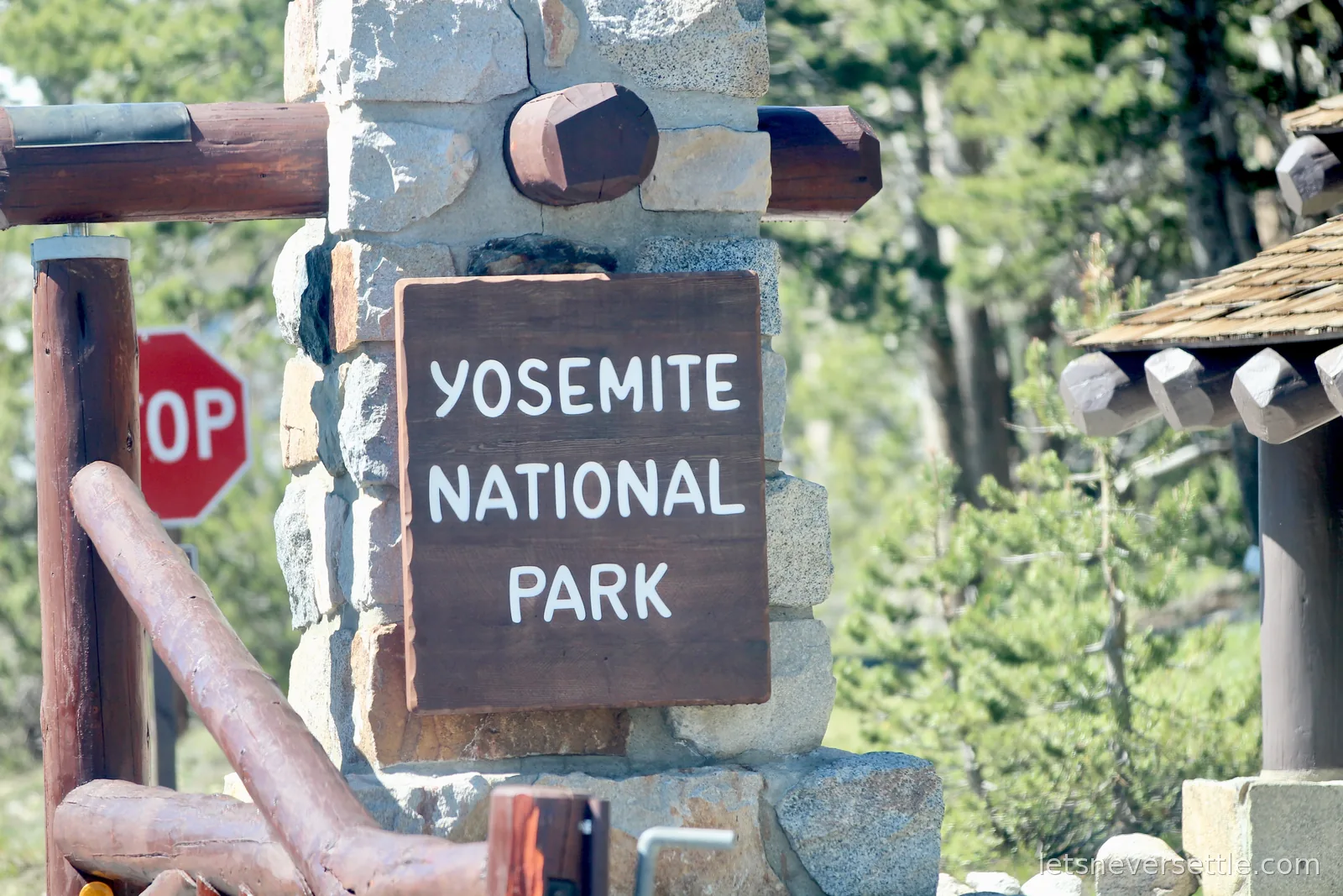 Yosemite National Park entrance sign mounted on a stone pillar beside a stop sign