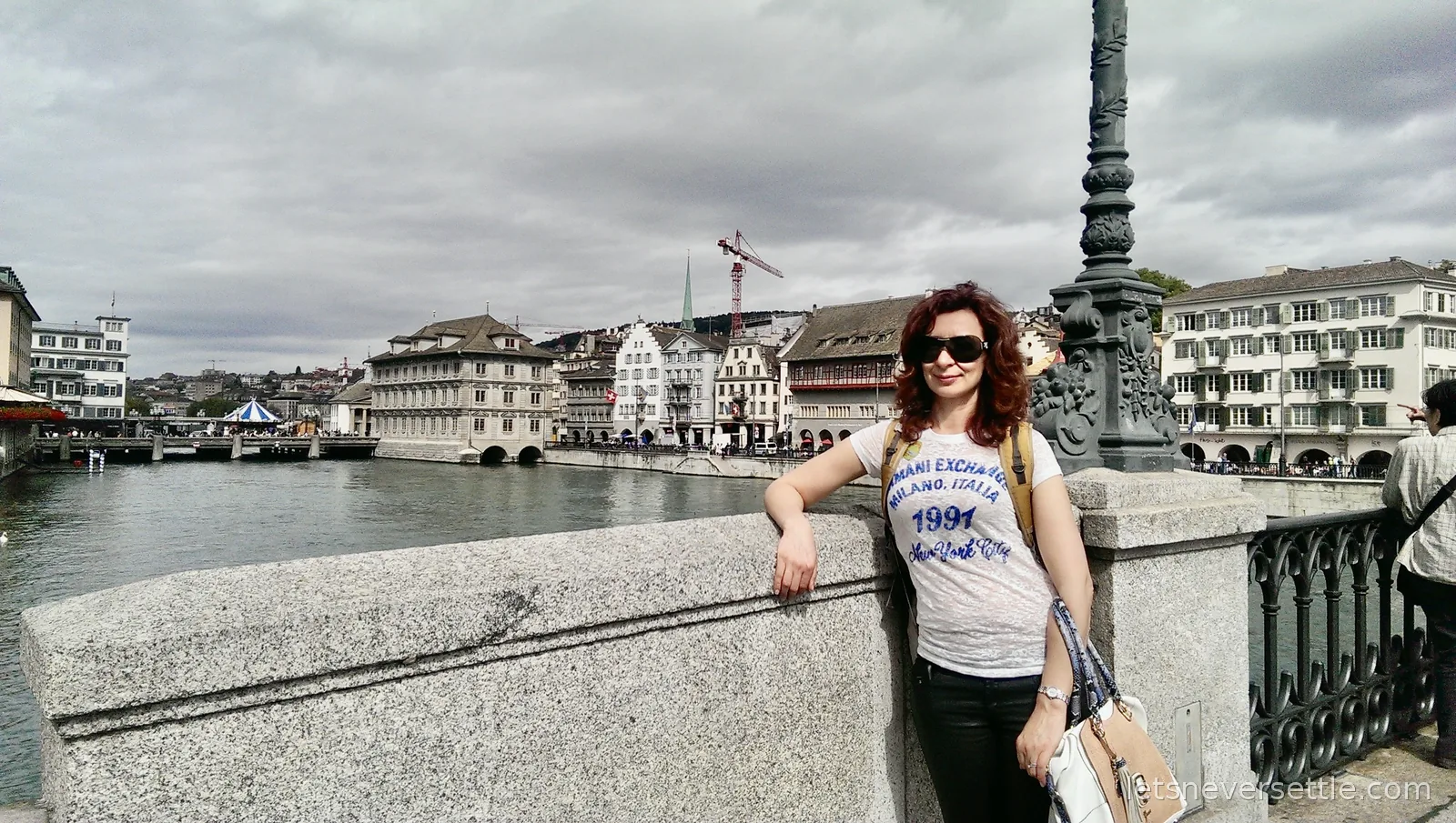 Inga leaning on the stone parapet of a bridge over the Limmat, the gabled houses of Zurich old town behind
